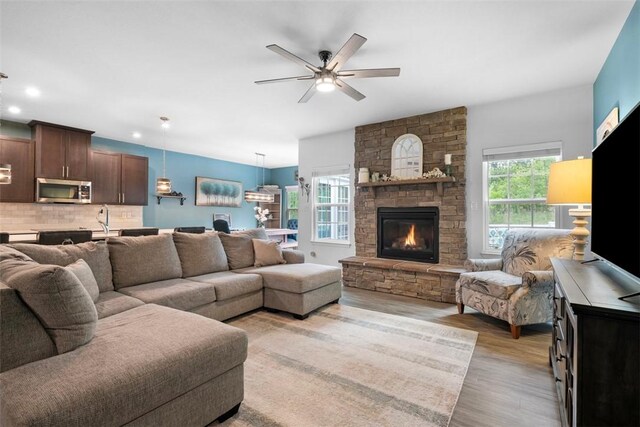 living room featuring light wood finished floors, ceiling fan, a stone fireplace, and recessed lighting