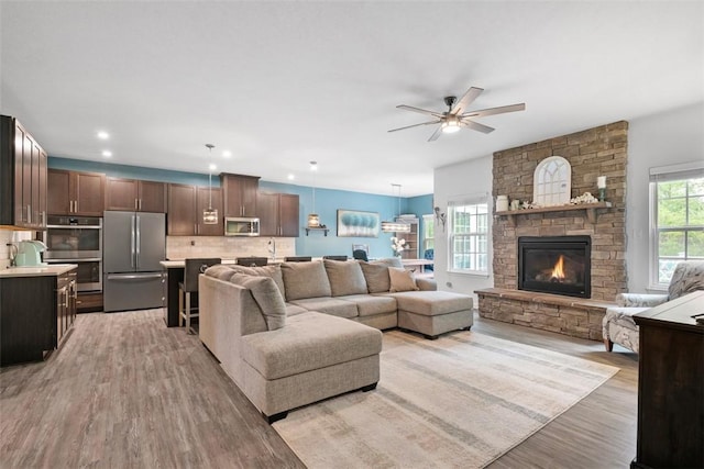 living area featuring light wood-style flooring, ceiling fan, and a stone fireplace