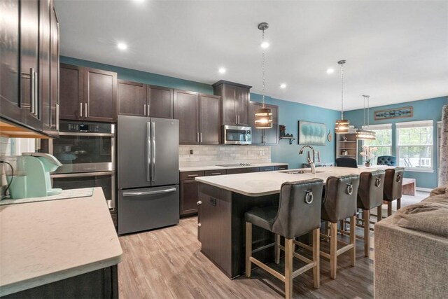 kitchen featuring appliances with stainless steel finishes, a sink, light countertops, dark brown cabinets, and backsplash