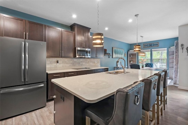 kitchen with stainless steel appliances, a sink, light wood finished floors, dark brown cabinets, and tasteful backsplash