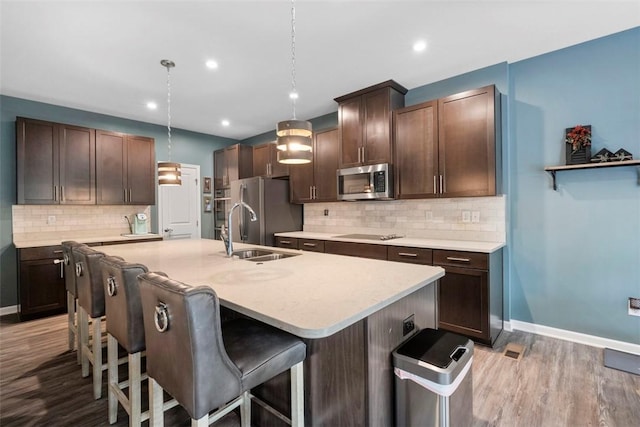 kitchen with appliances with stainless steel finishes, a sink, a breakfast bar area, tasteful backsplash, and wood finished floors
