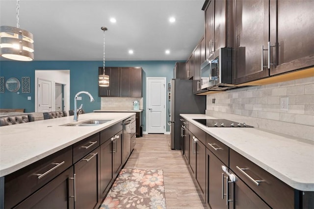 kitchen with a sink, dark brown cabinets, tasteful backsplash, light wood-style floors, and pendant lighting