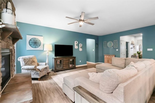 living area with wood finished floors, ceiling fan, a fireplace, and baseboards