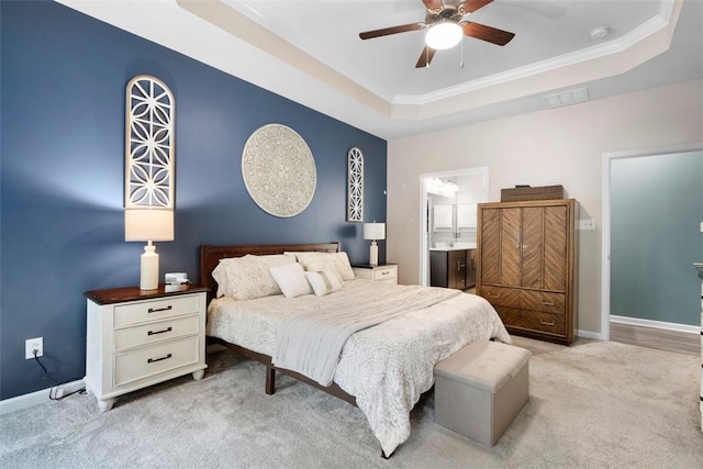 carpeted bedroom featuring a raised ceiling, baseboards, crown molding, ceiling fan, and ensuite bath