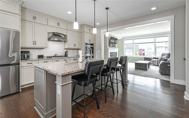 kitchen featuring stainless steel appliances, a kitchen breakfast bar, open floor plan, light stone countertops, and tasteful backsplash