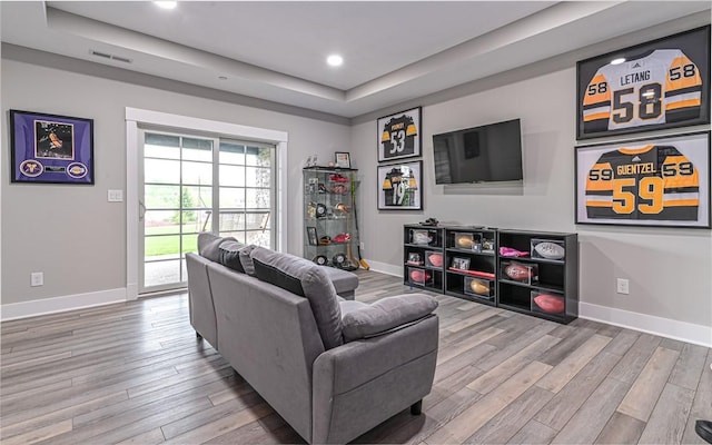 living area with wood finished floors, baseboards, a raised ceiling, and recessed lighting
