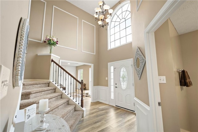 entryway with a chandelier, wood finished floors, a decorative wall, a wainscoted wall, and stairs