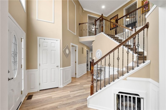 foyer entrance with a towering ceiling, wood finished floors, wainscoting, stairs, and ornamental molding