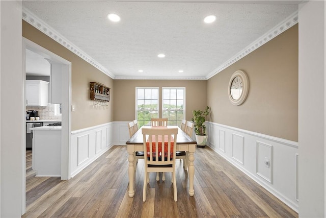 dining space featuring a decorative wall, wainscoting, wood finished floors, recessed lighting, and a textured ceiling