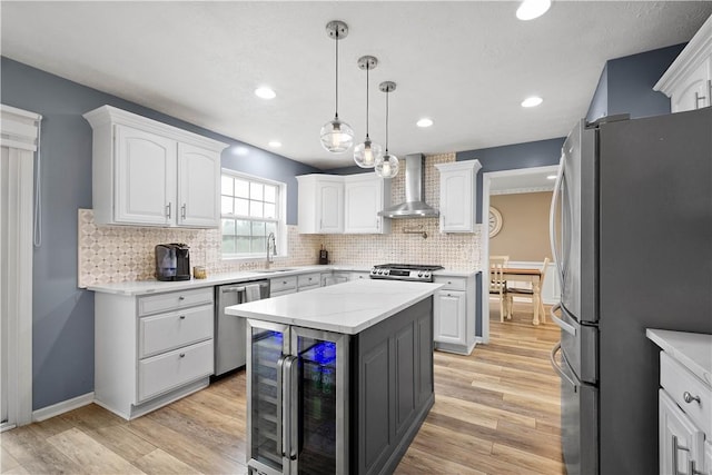 kitchen with stainless steel appliances, wall chimney exhaust hood, wine cooler, a sink, and white cabinetry