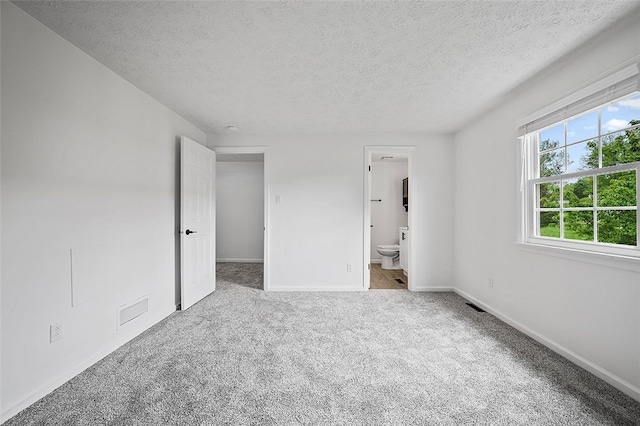 unfurnished bedroom with a textured ceiling, carpet flooring, baseboards, and ensuite bath