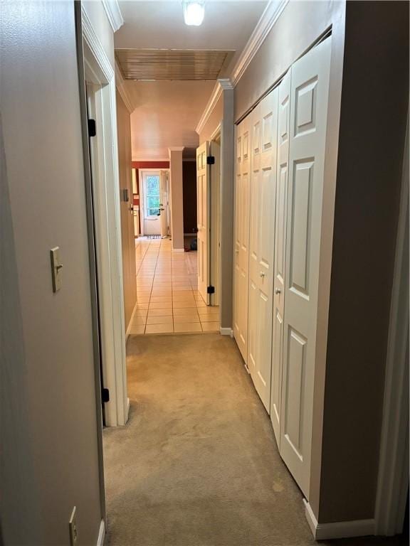 hallway featuring crown molding, light colored carpet, and light tile patterned floors