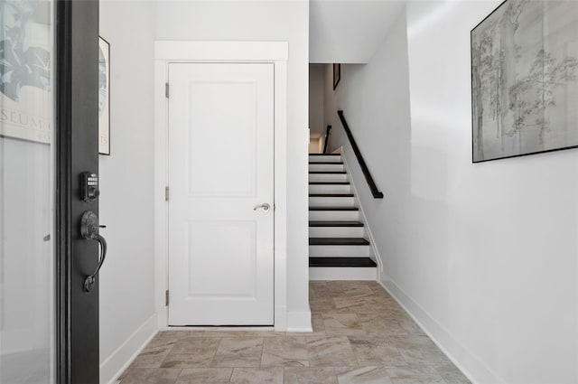 foyer featuring baseboards, light marble finish flooring, and stairs
