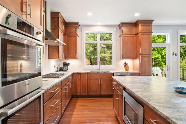 kitchen featuring stainless steel appliances, a sink, recessed lighting, brown cabinets, and light wood-type flooring