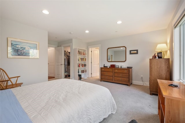 bedroom with light colored carpet, recessed lighting, baseboards, a walk in closet, and a closet