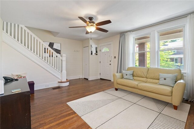living area with a ceiling fan, wood finished floors, stairs, and baseboards
