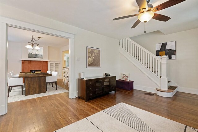 living room featuring wood finished floors, stairs, a fireplace, ceiling fan, and baseboards