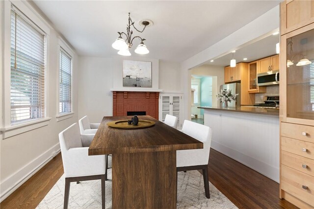 dining space with dark wood-type flooring, a chandelier, baseboards, a fireplace, and recessed lighting