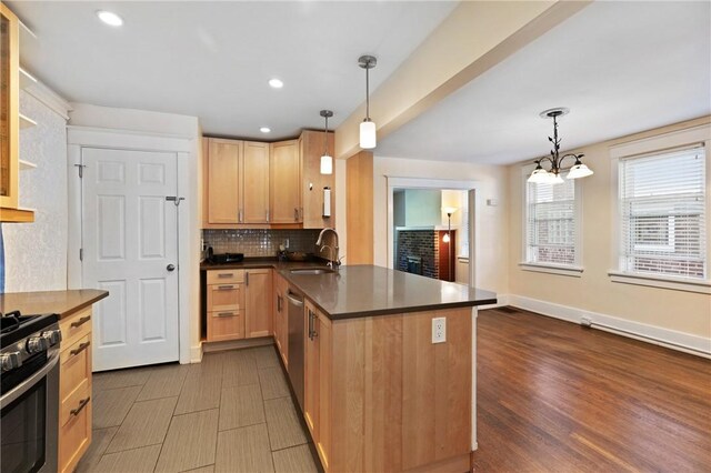 kitchen with a sink, stainless steel appliances, a peninsula, dark wood-style flooring, and backsplash