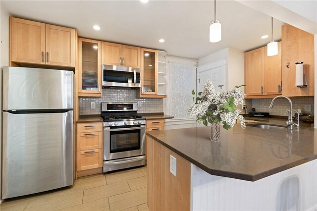 kitchen with appliances with stainless steel finishes, a sink, a peninsula, decorative backsplash, and glass insert cabinets