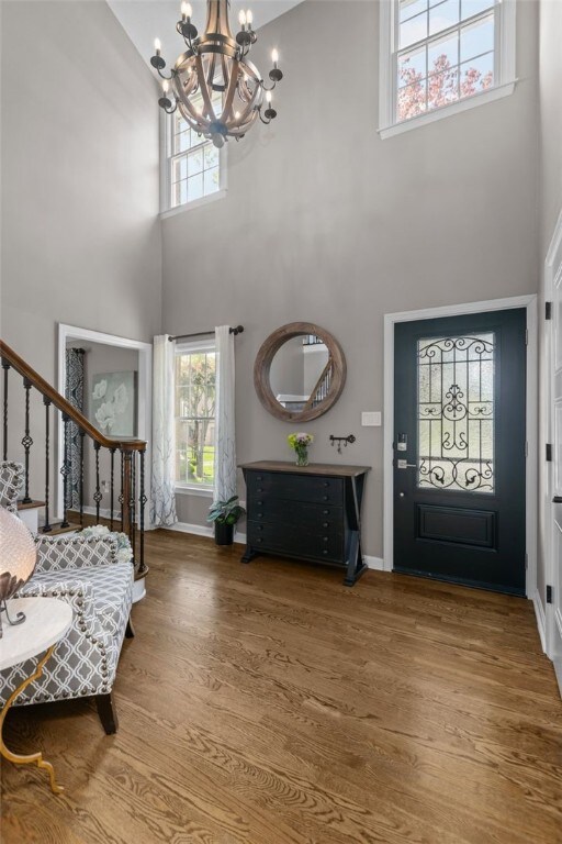 entryway with a chandelier, a towering ceiling, wood finished floors, healthy amount of natural light, and baseboards