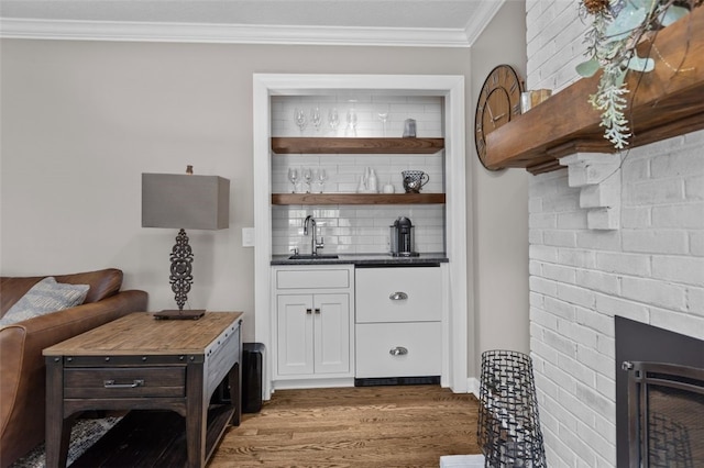 indoor wet bar featuring wood finished floors, a fireplace, decorative backsplash, and crown molding
