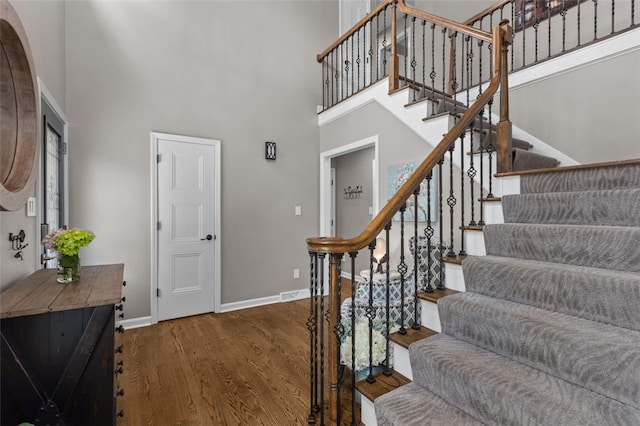 stairs with a high ceiling, wood finished floors, and baseboards