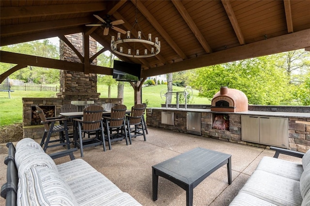view of patio / terrace with exterior kitchen, an outdoor stone fireplace, a ceiling fan, and a gazebo