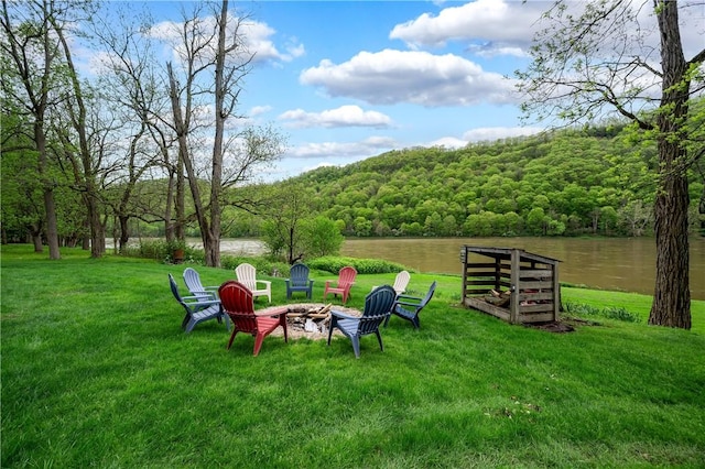 view of grassy yard with a view of trees, a fire pit, and a water view