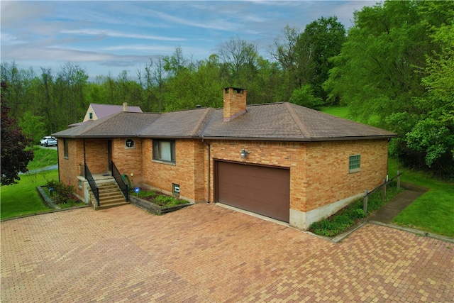 view of front of home featuring a chimney, brick siding, a garage, decorative driveway, and roof with shingles
