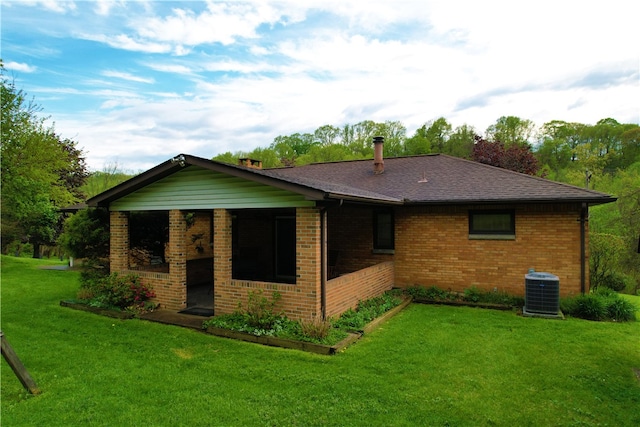 rear view of property featuring brick siding, a yard, roof with shingles, and central air condition unit
