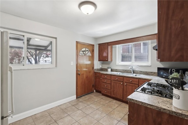 kitchen with a sink, light tile patterned floors, baseboards, brown cabinetry, and range with gas stovetop