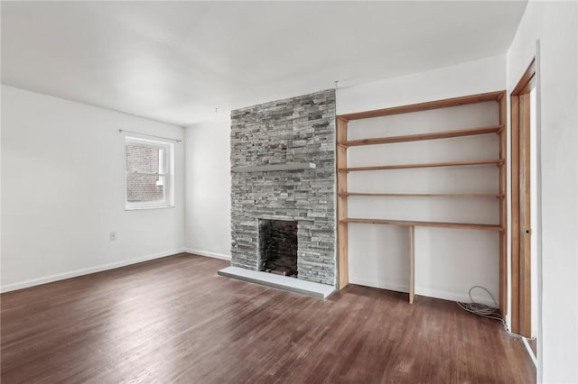 unfurnished living room featuring wood finished floors, a stone fireplace, and baseboards