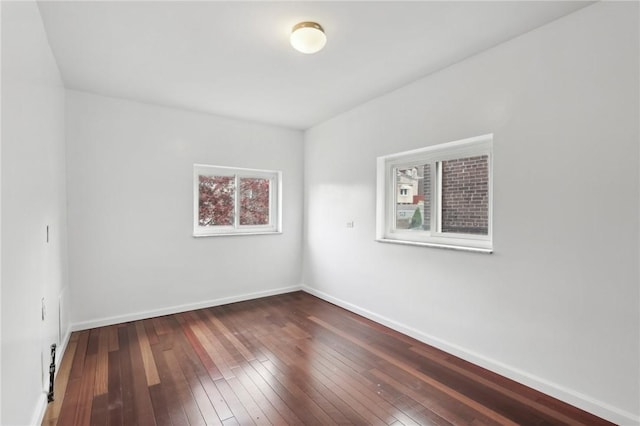 unfurnished room featuring healthy amount of natural light, wood-type flooring, and baseboards