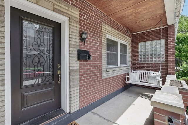 doorway to property featuring a porch and brick siding