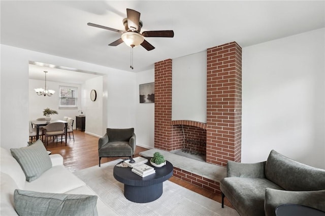 living area with a ceiling fan, wood finished floors, a chandelier, and a fireplace