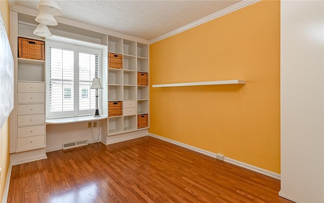 empty room with crown molding, wood finished floors, baseboards, and a textured ceiling