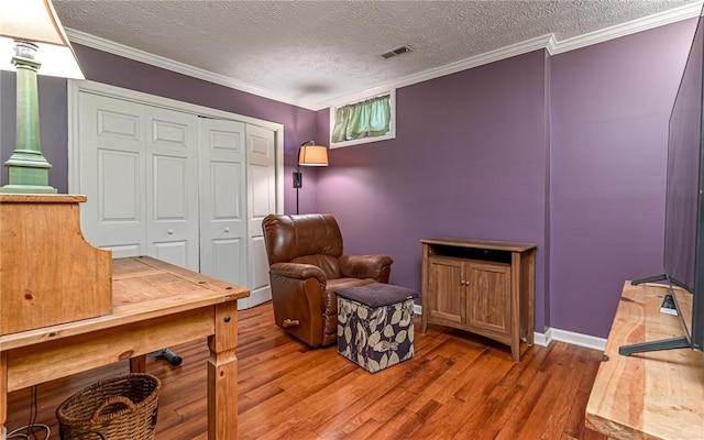 living area featuring hardwood / wood-style floors, ornamental molding, a textured ceiling, and ornate columns