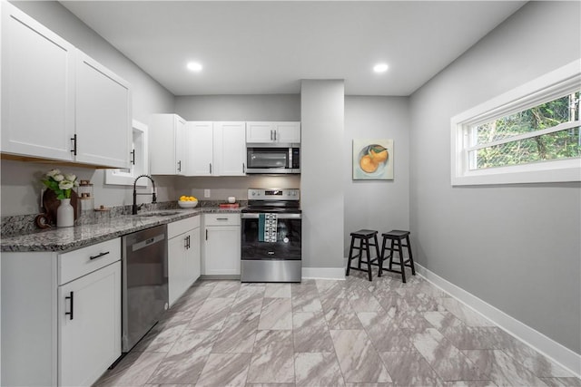 kitchen featuring appliances with stainless steel finishes, a sink, stone counters, white cabinets, and baseboards