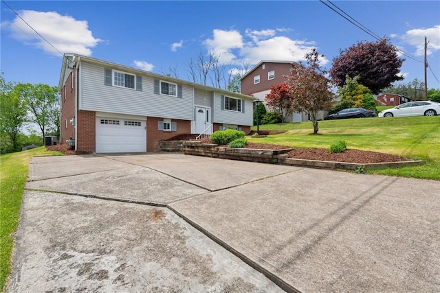 raised ranch featuring brick siding, a garage, a front yard, and driveway