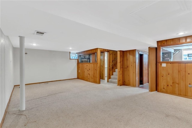 below grade area featuring stairs, light carpet, wooden walls, and baseboards