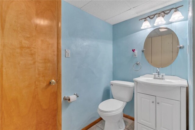 half bath with toilet, a paneled ceiling, tile patterned floors, vanity, and baseboards