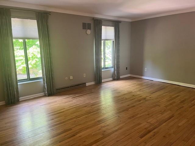 spare room with ornamental molding, a baseboard heating unit, healthy amount of natural light, and wood finished floors