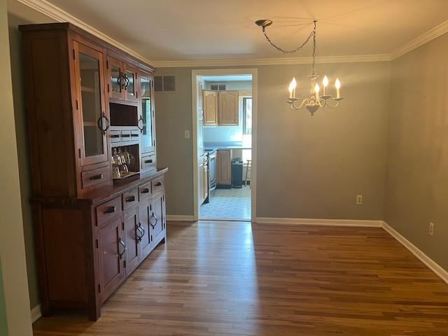 unfurnished dining area with a chandelier, wood finished floors, ornamental molding, and baseboards