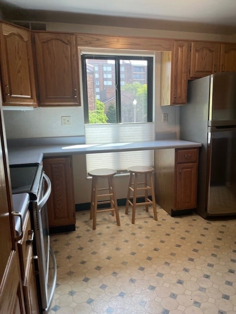 kitchen with appliances with stainless steel finishes, light floors, brown cabinets, and light countertops