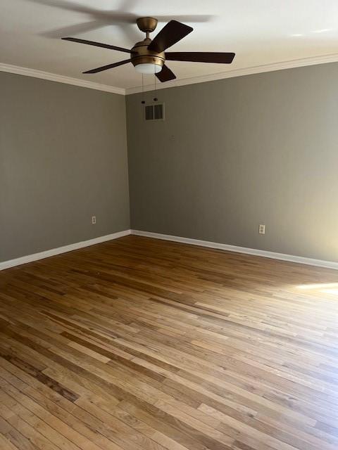 spare room with ornamental molding, wood-type flooring, a ceiling fan, and baseboards