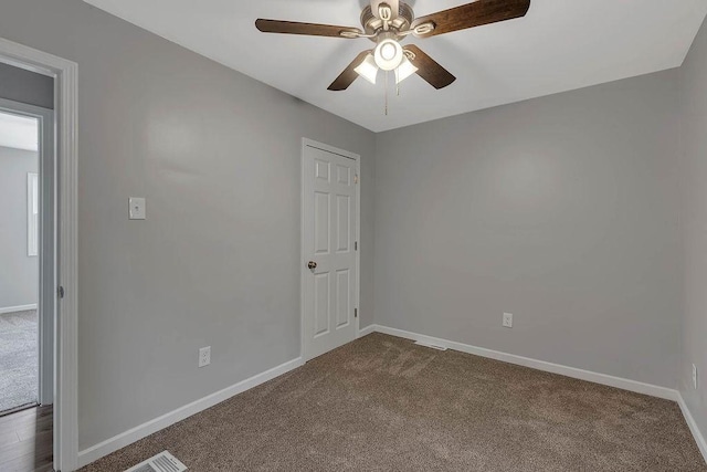 empty room featuring dark carpet, a ceiling fan, and baseboards