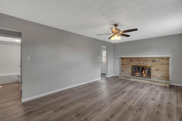 unfurnished living room with a textured ceiling, a ceiling fan, wood finished floors, a stone fireplace, and baseboards