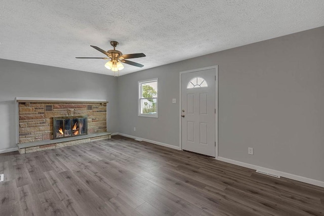 unfurnished living room with a textured ceiling, wood finished floors, baseboards, ceiling fan, and a stone fireplace