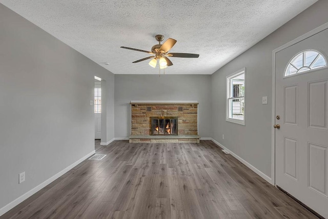 unfurnished living room with a textured ceiling, wood finished floors, ceiling fan, baseboards, and a fireplace